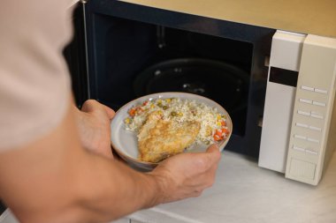 Yemek tabağını mikrodalgaya koyan adam, yakın plan.