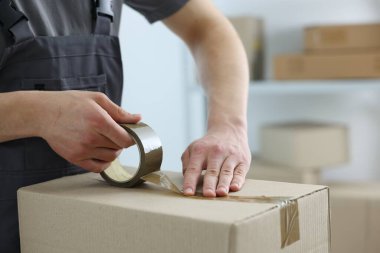 Kapalı alanda yapıştırıcı bantlı karton kutu mühürleyen adam.