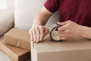 Kapalı alanda yapıştırıcı bantlı karton kutu mühürleyen adam.