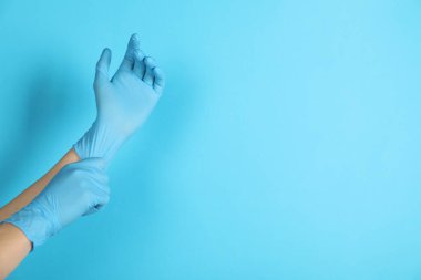 Doktor açık mavi arka plana tıbbi eldiven takıyor, yakın plan. Metin için boşluk