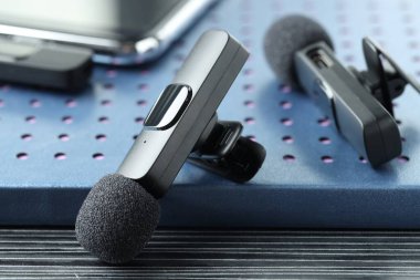 Lavalier mikrofonlar, kablosuz alıcısı olan akıllı telefon ve siyah ahşap masadaki defter, yakın plan.