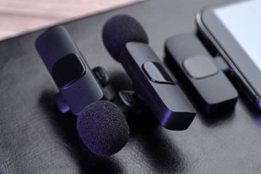 Lavalier mikrofonlar, kablosuz alıcısı ve siyah defteri olan akıllı telefon, yakın plan.