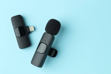 Lavalier mikrofon ve açık mavi arkaplanda kablosuz alıcı, düz konum. Metin için boşluk