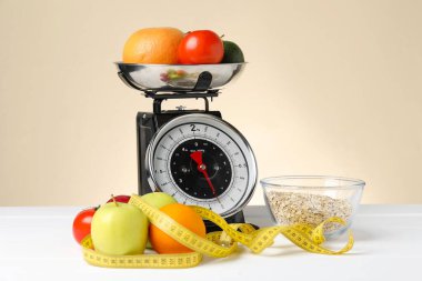 Ürünlerle birlikte mekanik mutfak terazisi ve bej arka planda beyaz ahşap masadaki şerit. Diyet