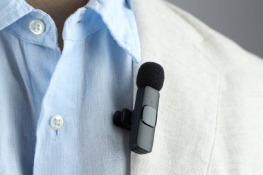 Gri arka planda takım elbisesine mikrofon takmış bir adam, yakın plan.