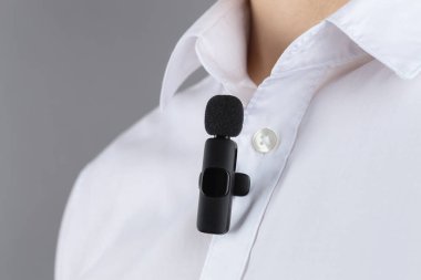 Gri arka planda gömleğine mikrofon takmış bir adam.