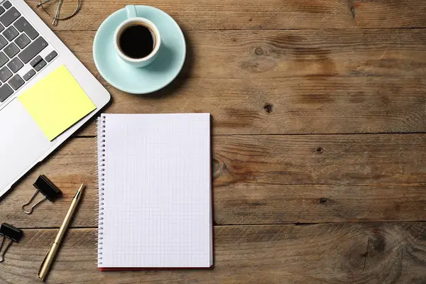 Kalemli defter, yapışkan not, dizüstü bilgisayar, ataç ve tahta sehpada kahve. Metin için boşluk