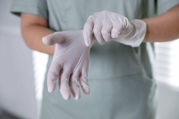 Medical worker putting on gloves in hospital, closeup