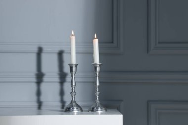 Modaya uygun şamdanlar, kapalı alandaki gri duvarın yanındaki beyaz çekmecelerin üzerinde yanan mumlar.