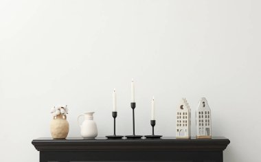 Beyaz duvarın yanındaki şöminede yanan mumlar ve diğer dekorlarla süslü şamdanlar.