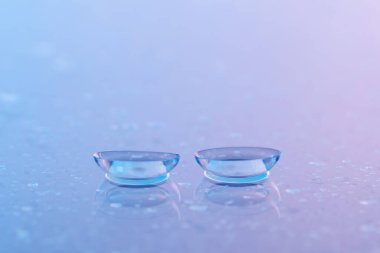 Bir çift kontakt lens ve su damlası mor ayna yüzeyine düşer, yakın plan.