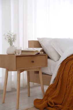 İçinde kitap olan komodin, vazoda çiçekler, yatağın yanında bir bardak su ve bardaklar.