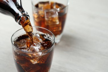 Açık gri masada şişeden cama ferahlatıcı kola dökülüyor, yakın plan. Metin için boşluk