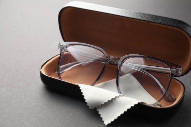 Gri arka planda şık gözlüklü ve temizlik bezli çanta, yakın plan.