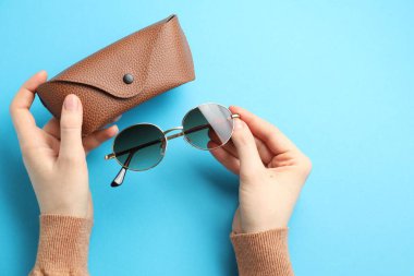 Güneş gözlüklü ve açık mavi arka planda çantası olan bir kadın. Metin için boşluk