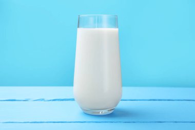 Açık mavi ahşap masada cam içinde taze süt.