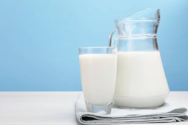 Bardakta taze süt ve açık mavi arka planda beyaz ahşap masada sürahi. Metin için boşluk