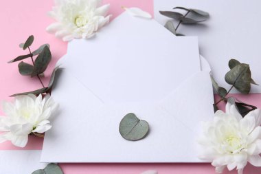 Kağıt zarftaki boş tebrik kartı, kasımpatı çiçekleri ve pembe arkaplanda okaliptüs dalları, yakın plan.