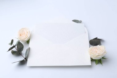 Zarfta boş tebrik kartı, okaliptüs yaprakları ve beyaz arka planda güller