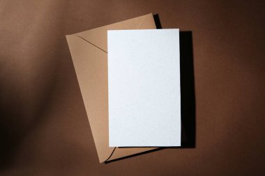 Kahverengi arkaplanda boş tebrik kartı ve kağıt zarf, üst görünüm