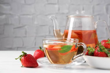 Aromatik meyve çayı, çilek ve nane şekeri beyaz mermer masada, yakın plan.