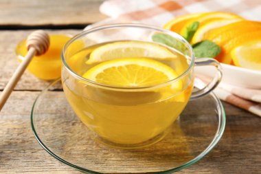 Cam fincanda aromatik meyve çayı, portakal, limon, bal ve nane, ahşap masada, yakın plan.