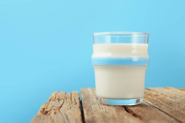 Açık mavi arka planda, cam bardakta, tahta masada taze süt, yakın plan. Metin için boşluk