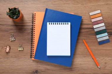 Kalem, not defterleri, renkli çıkartmalar, cilt tokaları ve tahta masa üzerindeki çiçek dekoru.