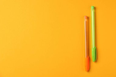 Turuncu arka planda şık kalemler, üst manzara. Metin için boşluk