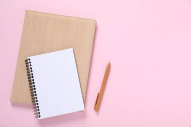 Kalem ve defterler pembe arka planda, düz yatıyordu. Metin için boşluk
