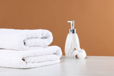 Temiz havlular, kozmetik ürünler ve pamuk çiçekleri kahverengi arka planda.