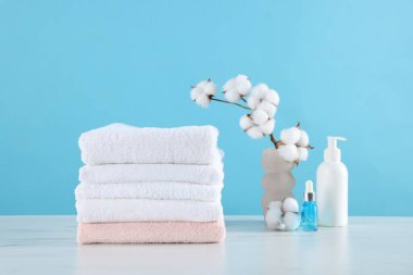 Temiz havlular, pamuk çiçekleri ve kozmetik ürünleri beyaz mermer masa üzerinde açık mavi arka plan