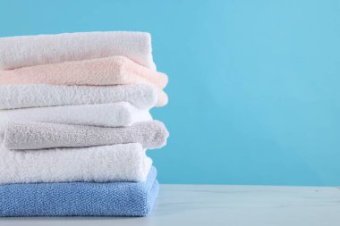 Açık mavi arka planda beyaz mermer masaya temiz havlu yığını, yakın plan. Metin için boşluk