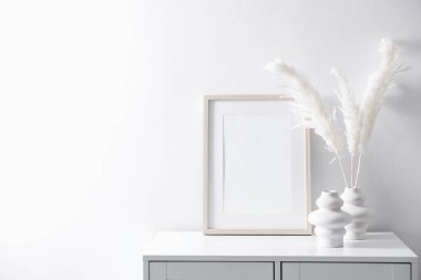 Beyaz duvarın yanındaki dolapta boş resim çerçevesi ve şık ev dekorasyonu