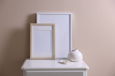 Boş resim çerçeveleri, vazo ve mücevherler bej duvarın yanındaki dolapta.