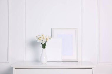 Vazodaki güzel nergisler ve evdeki beyaz duvarın yanındaki dolaptaki resim çerçeveleri.