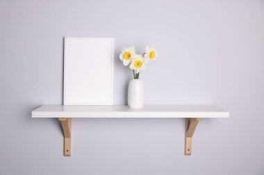 Vazodaki güzel nergisler ve içerideki beyaz raftaki resim çerçevesi