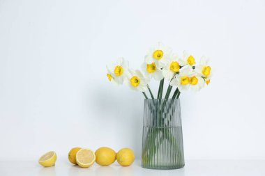 Vazodaki güzel nergisler ve beyaz masadaki limonlar.