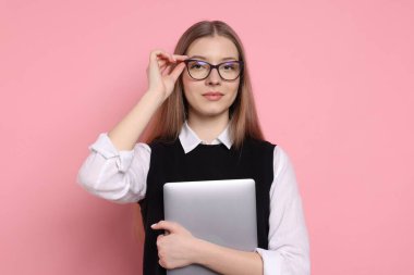 Pembe arka planda dizüstü bilgisayarı olan güzel bir genç kız.