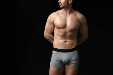 Siyah arka planda açık gri iç çamaşırlı genç adam, yakın plan.