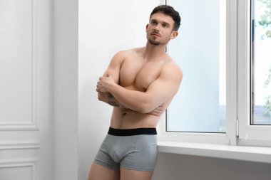Beyaz duvarın yanında şık, açık gri iç çamaşırlı genç adam.