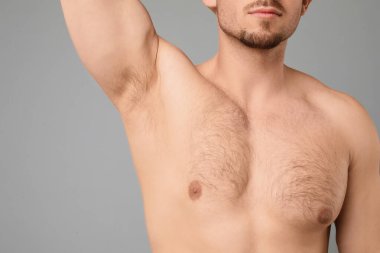 Genç adam açık gri arka planda kıllı koltukaltını gösteriyor, yakın plan. Epilasyon işlemi