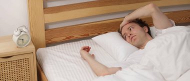 Yatakta çalar saate bakan uyuyakalmış bir adam.