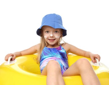 Cildinde güneş kremi ve beyaz arka planda şişme yüzük olan gülümseyen küçük bir kız.