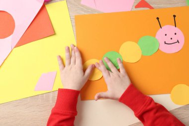 Küçük kız ahşap masada renkli kağıtlarla el yapımı bir proje yapıyor.