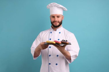 Üniformalı mutlu pastacı açık mavi arka planda lezzetli ekinler tutuyor.