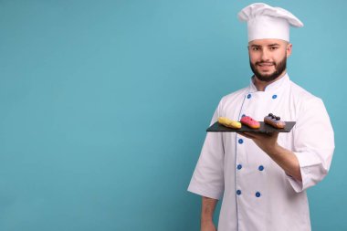 Üniformalı mutlu pastacı açık mavi arka planda lezzetli ekinler tutuyor, mesaj için yer var.