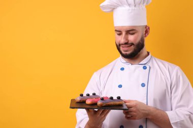 Üniformalı mutlu pastacı turuncu arka planda ekinler tutuyor.