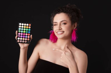 Gülümseyen kadın, siyah arka plandaki parlak göz falı paletine işaret ediyor.