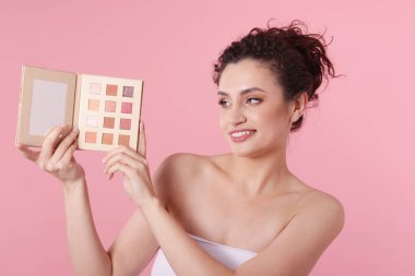 Pembe arka planda göz farı paleti olan gülümseyen kadın.